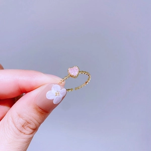 Nahaufnahme eines goldenen Rings mit rosa Glitzerherz auf fliederfarbenem Hintergrund