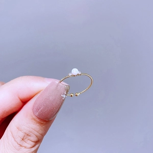 Detail eines Goldrings mit weißem Opal und Zirkonia auf lilafarbenem Hintergrund