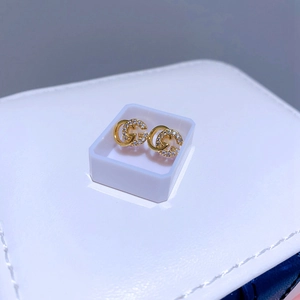 Detailaufnahme goldener Ohrstecker mit ineinandergreifendem G-Design und Zirkonia-Besatz