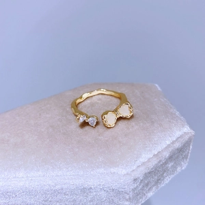Dettaglio di un anello aperto dorato con zirconi a cuore e design in smalto bianco