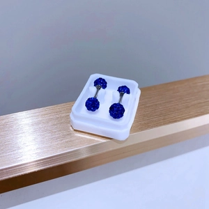 Detail shot of blue crystal pavé ball earrings in a white box on a golden edge