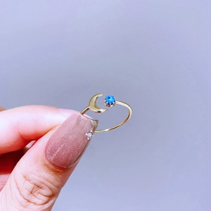 Nahaufnahme des goldenen Mondsichel-Rings mit rundem blauem Edelstein vor blauem Grund