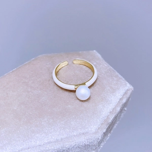 Dettaglio macro di un anello dorato regolabile con smalto bianco e una perla lucida