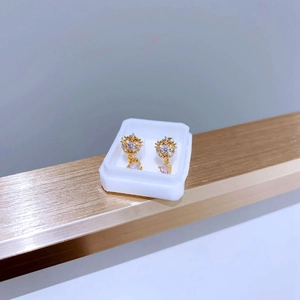 Detailansicht goldener Titan-Ohrringe mit klaren Steinen und rosa Herzanhängern
