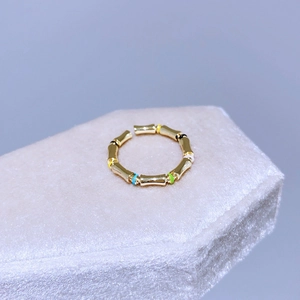 Dettaglio dell'anello dorato stile bambù con perle smaltate colorate su base in velluto