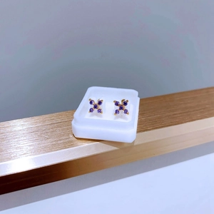 Nahaufnahme von X-förmigen Goldohrringen mit lila Zirkonia in einer kleinen Box