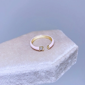 Dettaglio di un anello aperto in smalto rosa con fascia dorata e zircone rettangolare