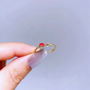 Detail of gold open ring with red enamel mushroom and cubic zirconia accents