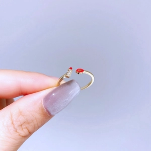 Detail of gold open ring featuring red lips and lipstick motif with sparkling zircons