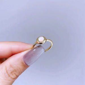 Detail of gold textured ring featuring a shimmering round opal stone held by fingers