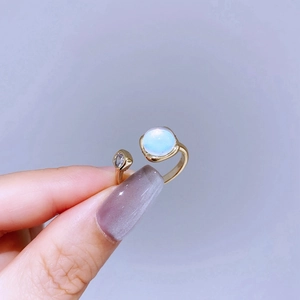 Detail of a gold open ring featuring a blue moonstone and a sparkling zircon on a finger