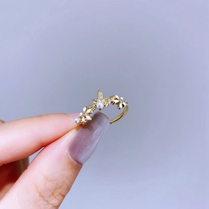 Close-up of golden open ring featuring white enamel flowers, butterfly and pearls