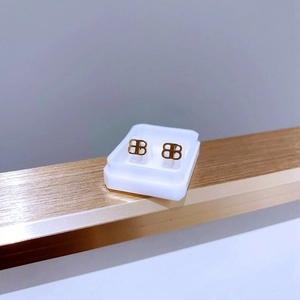 Detail der goldenen Titan-Ohrstecker mit Doppel-B-Logo auf einem Metallständer