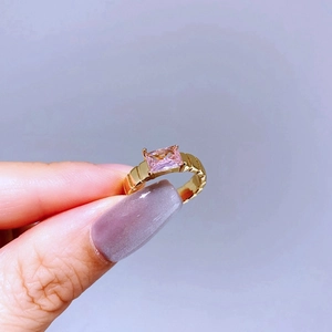 Detail of gold ring featuring a rectangular pink gemstone with geometric band texture