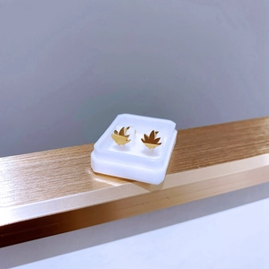 Detailansicht goldener Blatt-Ohrstecker in weißer Box auf einem goldenen Ständer