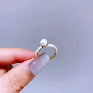 Detail of elegant gold ring featuring white enamel surface and a single lustrous pearl