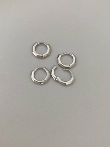 Makro-Detail von zwei Paar silberfarbenen, sechseckigen geometrischen Creolen mit poliertem Finish