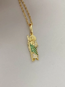 Detalle del colgante de Jesús dorado con cristales verdes y blancos en una cadena de cruz