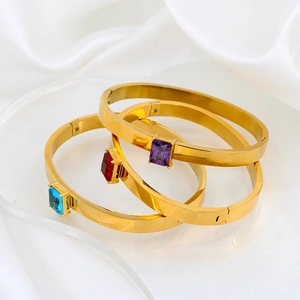 Tres brazaletes de acero dorado con circonitas rojas, moradas y azules sobre satén