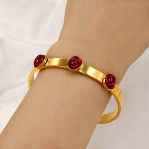 Detail of 18k gold plated stainless steel open bangle with three red oval gemstones