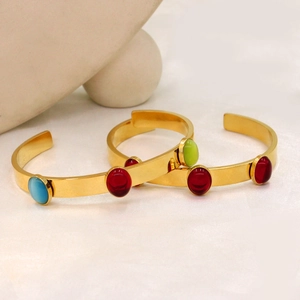 Polished 18k gold plated cuffs with colorful oval stones on minimalist rock background