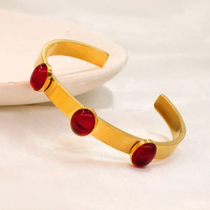 Close-up of gold-plated open bangle with three red oval gemstones on silk background
