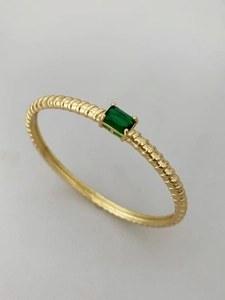 Dettaglio anello dorato a spirale con zircone verde rettangolare e incastonatura a 4 griffe