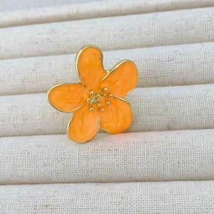 Macro view of bright orange camellia ring with gold trim in a beige jewelry tray