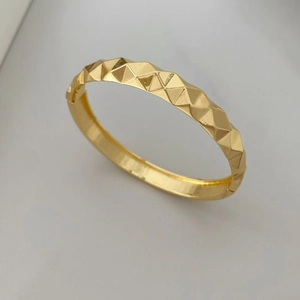 Detalle de brazalete de metal dorado con facetas geométricas y acabado pulido brillante