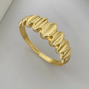 Detalle de un brazalete rígido dorado con diseño de cuentas gruesas y acabado pulido