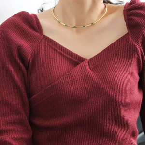 Gros plan sur le collier ras de cou doré orné de zircons rectangulaires vert émeraude