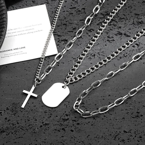 Collar multicapa de acero de titanio con colgante de cruz y placa sobre fondo de piedra rugosa