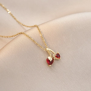 Détail du collier cerise doré avec pierres rouges en cœur sur fond de soie