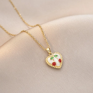 Détail macro d'un pendentif cœur doré avec cerise en émail sur fond de soie douce