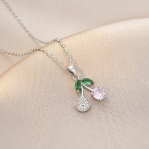 Détail du collier pendentif cerise avec pierres roses et vertes sur soie champagne