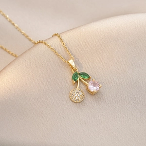 Détail du collier cerise avec pierre rose, feuilles vertes et chaîne dorée croisée