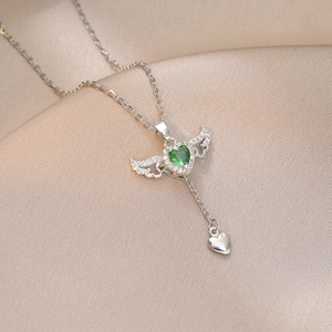 Detail of angel wing heart necklace with green zircon on elegant champagne silk fabric