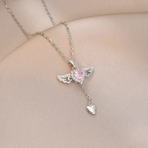 Detail of silver angel wing heart necklace with pink zircon on champagne silk fabric