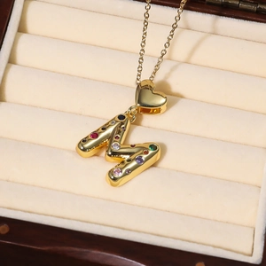 Makroaufnahme von goldenem Buchstaben-M-Anhänger mit bunten Steinen und Herz-Öse