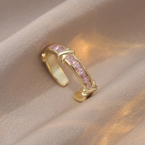 Détail d'une bague dorée avec zircons roses et texture de corde croisée