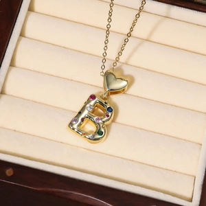 Detailaufnahme des goldenen Herzens und B-Anhängers mit bunten Zirkonia in einer Box