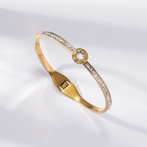 Detail of gold titanium bangle with pavé rhinestones and a white starburst flower charm