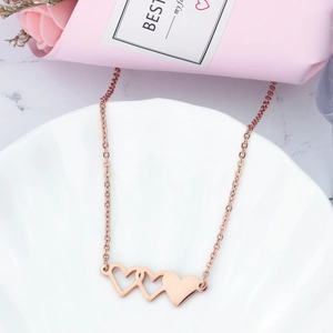 Gros plan du collier à trois cœurs entrelacés en or rose posé sur un plateau décoratif