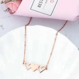 Détail du collier trois cœurs en or rose posé sur un plateau décoratif en céramique