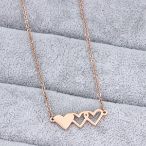 Détail du collier rose doré à trois cœurs sur plateau de velours gris, finition polie