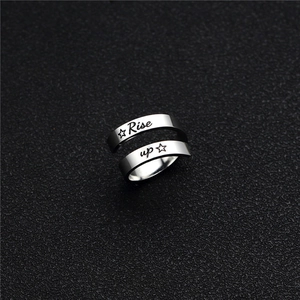 Gros plan détaillé d'une bague argentée gravée Rise Up et étoiles sur fond noir