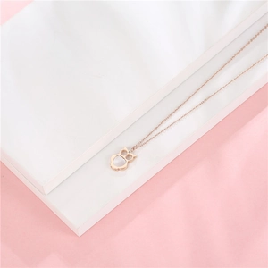 Detail of rose gold owl necklace with white shell inlay and zircon eye on pink backdrop