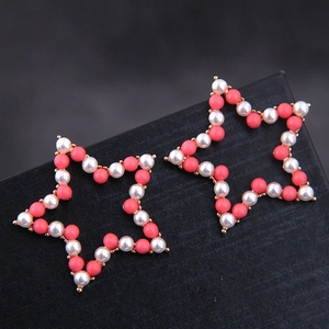 Boucles d'oreilles étoiles dorées avec perles blanches et corail sur boîte à bijoux