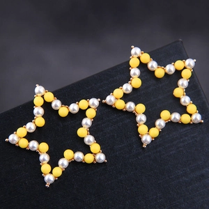 Boucles d'oreilles étoiles dorées ajourées avec perles blanches et jaunes sur fond noir