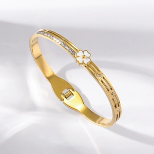 Detailed macro of gold-plated titanium bangle with zircon heart and white flower charms